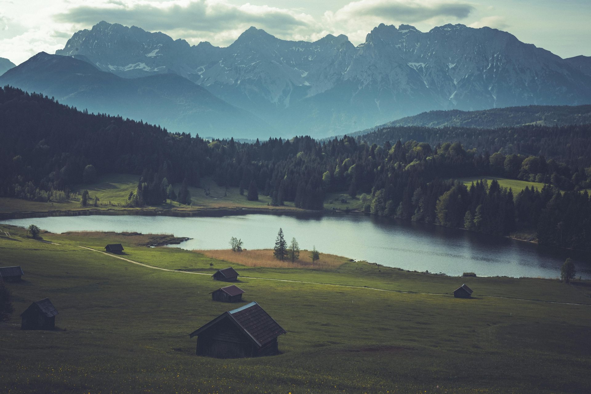 Ruhiger Blick auf die bayerischen Alpen mit Hütten an einem See und üppigem Grün, perfekt für Naturliebhaber.